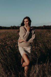 An example of a styled image used by a social media management client. Pictured is a woman with brown hair, wearing a neutral maxi skirt and jumper, in a field.