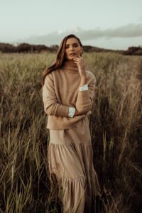 An example of a styled image used by a social media management client. Pictured is a woman with brown hair, wearing a neutral maxi skirt and jumper, in a field.