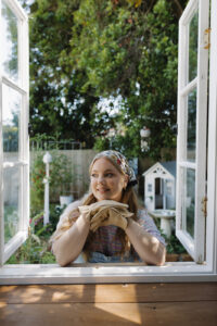 A woman with styled gardening clothes standing at the window.