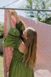 A woman in a green dress hanging out a pink sheet on the line.