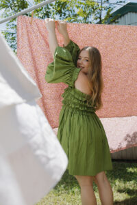 A woman in a green dress hanging out a pink sheet on the line.
