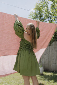 A woman in a green dress hanging out a pink sheet on the line.