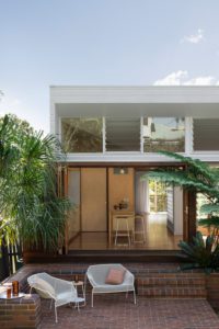 Facade of a modern home with a red brick exterior and louvre windows.