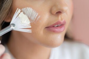 A close up shot of glowy skin getting a face mask applied with a brush.