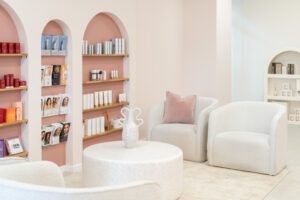 A modern boutique beauty clinic waiting room, featuring pink arched shelves and white boucle armchairs.