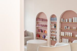 Arched pink shelves in a boutique beauty clinic waiting room, skincare products and brochures sit on them.