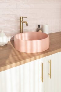 A pink basin with brass tap ware, pink subway tile backsplash, and oak bench tops.