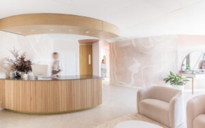 A boutique beauty clinic waiting room, featuring muted pink and oak tones, and indoor plants, and bespoke wallpaper.