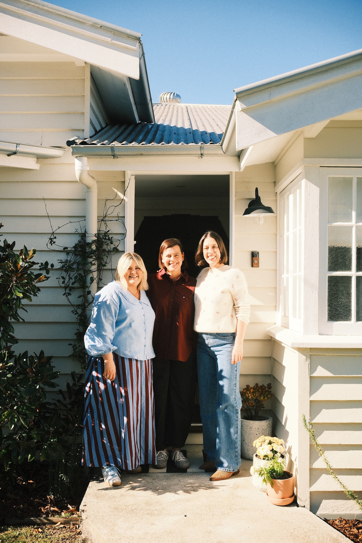 Three women standing at the entrance of a country style Queenslander home.