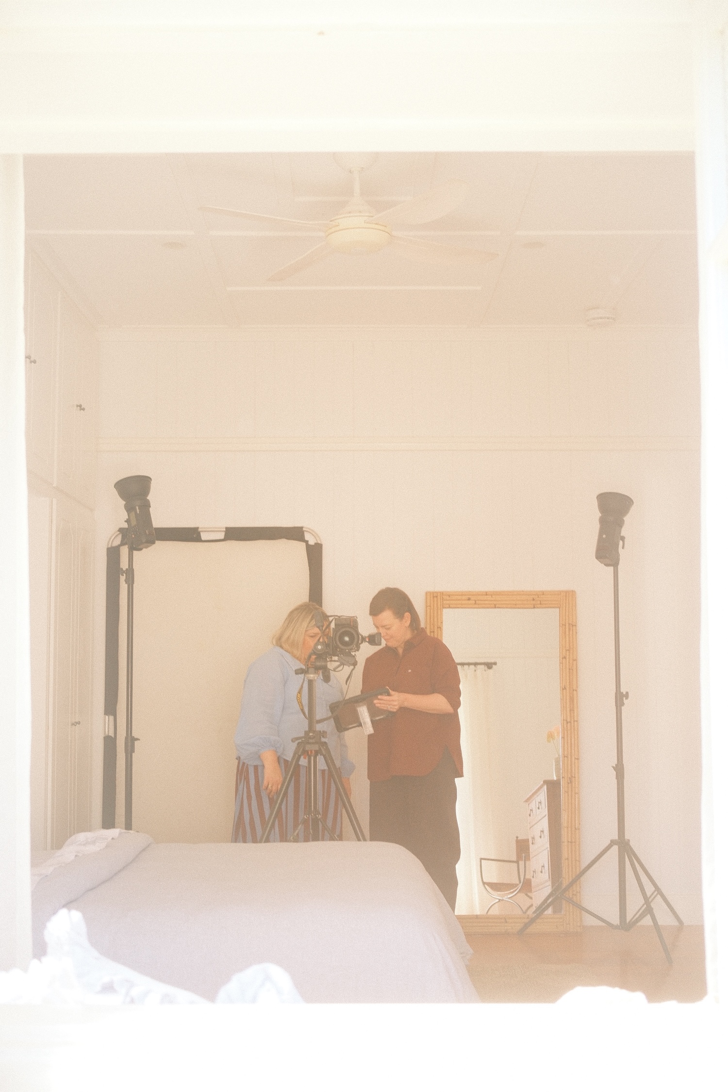 Two women working to style and photograph the primary bedroom of a country style Queenslander home.