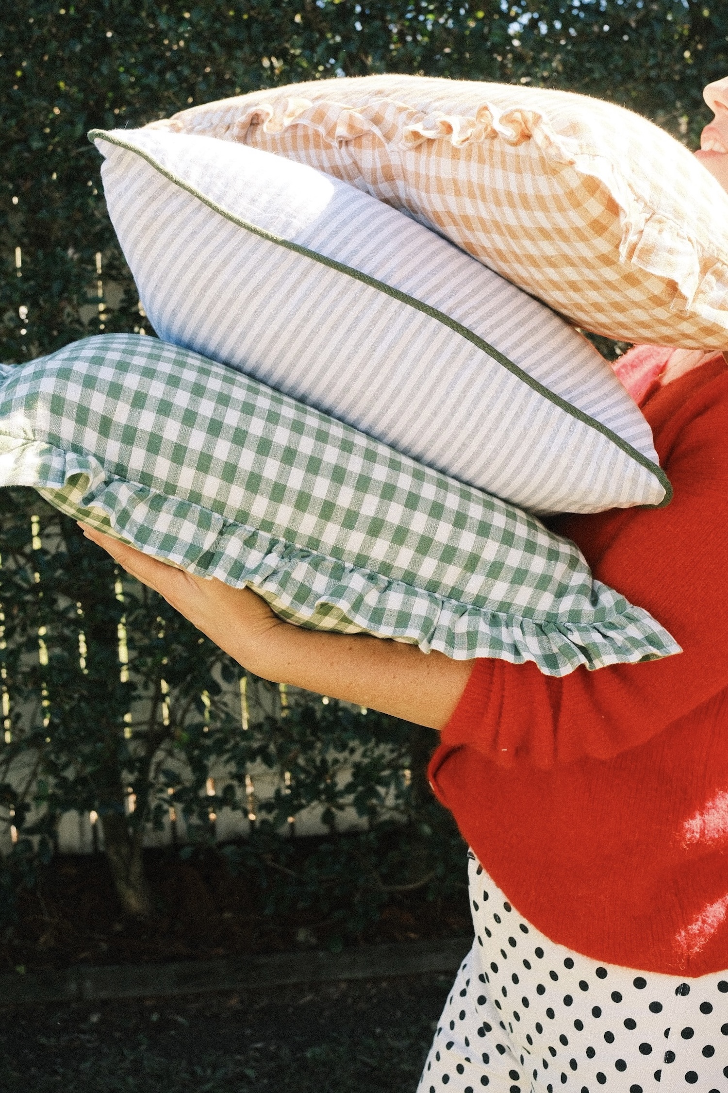 A woman in a red cardigan holding a stack of quality linen cushions.