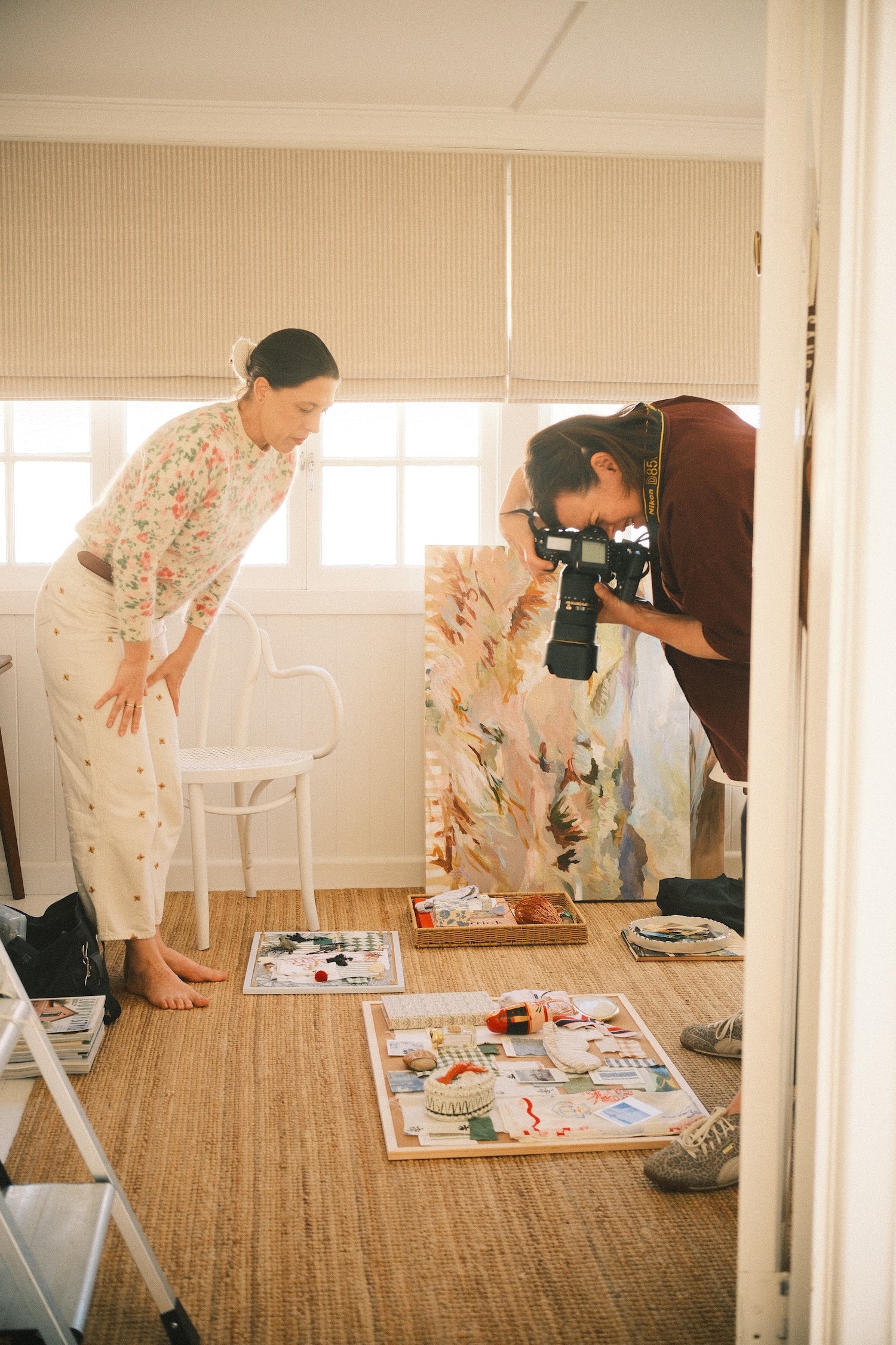 One lady looking down onto a curated mood board, while the other woman takes a photo.