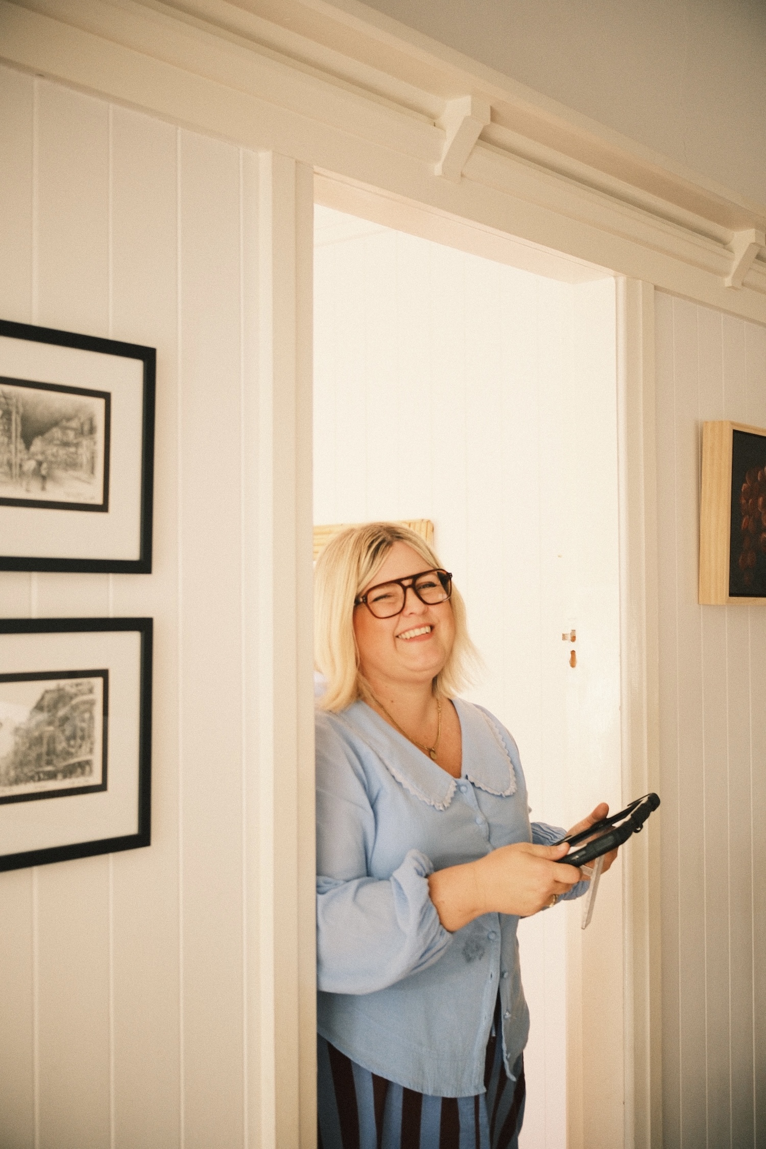 A woman in a blue shirt, holding a tablet, smiling at the camera.