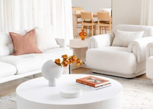 Modern lounge room with boucle arm chairs and sofas. Orchids sit in a ceramic vase on the coffee table.