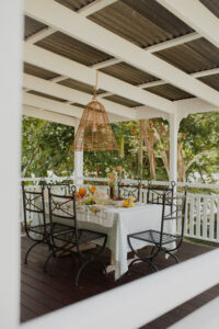 A festive spread covers an outdoor table on a renovated Queenslander veranda. There are fresh flowers, citrus fruits and bunches of grapes, and a pitcher of sparkling punch. Wrought iron dining chairs surround the table and a rattan pendant light hangs above it.