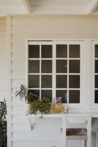A jug of lychee and elderflower sparkling punch sits on the bench of a renovated Queenslander veranda. Two vintage gold goblets sit beside it.