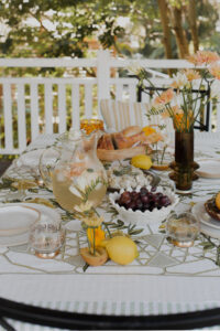 A festive spread covers an outdoor table on a renovated Queenslander veranda. There are fresh flowers and fruits, and a pitcher of sparkling punch.