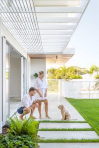 A couple out the front of their modern beach house with their dog.