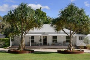 Exterior shot of a renovated white Queenslander home with pandanus trees in the foreground.