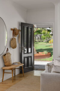The entrance of a renovated white country style Queenslander with an open black door and seat and wall rack styled with cane bags.