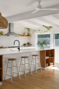 An angled shot of a white country style kitchen with three stools.