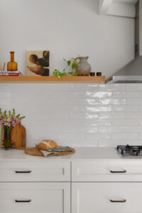 A white kitchen bench and drawers, styled with bread, vases and artwork.