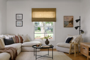 A wide shot of a living room in a renovated country style home with a while lounge and black coffee table, looking out a large window into the front yard.