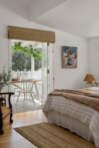 An angled shot of the guest bedroom opening out onto the verandah with table and chairs in a renovated country style home.