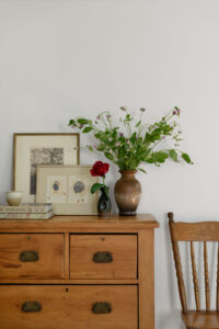 Wooden set of drawers with a wooden chair next to it with vases and picture frames styled on top.