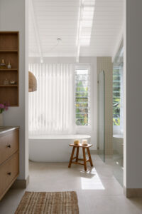Long shot of the bath with a wooden stool in front of it in the primary ensuite of a renovated country style Queenslander home.