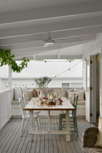 The back verandah of a white, renovated country style Queensland home with eclectic chairs around a table with afternoon tea served upon it.