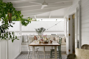 The back verandah of a white, renovated country style Queensland home with eclectic chairs around a table with afternoon tea served upon it.
