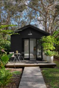 A narrow footpath leading to a black architectural guest house, surrounded by trees.