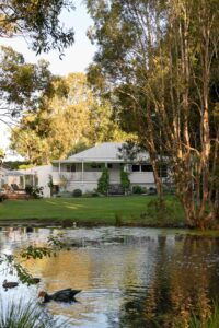 Exterior shot of a renovated white country style Queenslander home with lake in the foreground.