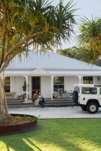 Exterior shot of a renovated white Queenslander home with pandanus trees in the foreground.