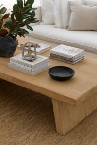 A close shot of a wooden coffee table with coffee table books, objects and greenery.