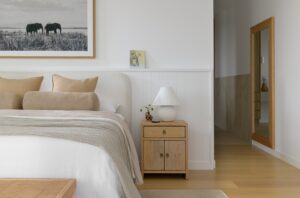 A modern primary suite with neutral ben linen and wooden bedside table with white lamp.