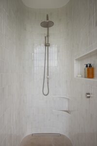 A modern shower space with floor to ceiling tiles.