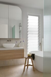A modern bathroom with neutral tiles and glass shutters.