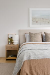 A modern bedroom styled with neutral bed linen and beach artwork.