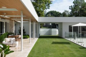 A modern outdoor living area styled with neutral furniture and glimpses of pool area and pool house.