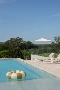 A modern Palm Springs inspired outdoor and pool area with green and white pool ring floating in pool, and umbrella and lounges on the pool's edge.