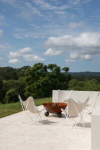 A modern outdoor fire pit styled with neutral outdoor chairs.