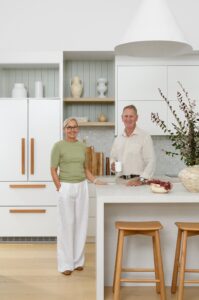Home owner couple stands in their new kitchen styled with vases and bowls.