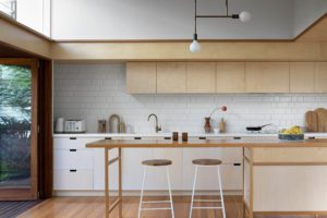 A modern kitchen with white wire stools and a plywood kitchen.