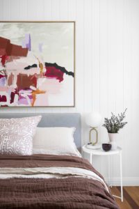 A modern bedroom with a Lucy Knox artwork, burgundy bedlinen, and decor from Trit.