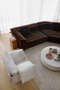 A bird's eye view of a modern cottage living area, featuring a brown velvet Sarah Ellison modular couch and a white linen armchair.