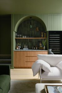 A moody bar downstairs in a modern cottage, painted entirely green. The couches and cushions are also green.