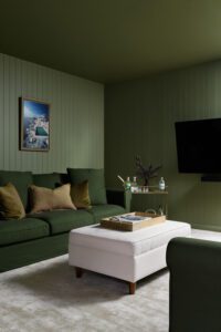 A moody bar downstairs in a modern cottage, painted entirely green. The couches and cushions are also green.