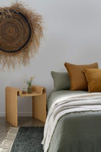 A bedroom with a khaki bed quilt and wall hanging.